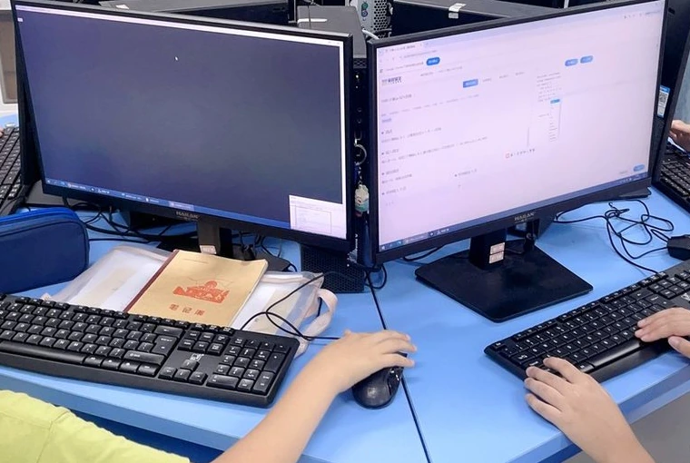 学生的双手在键盘和鼠标上操作，电脑显示编程界面