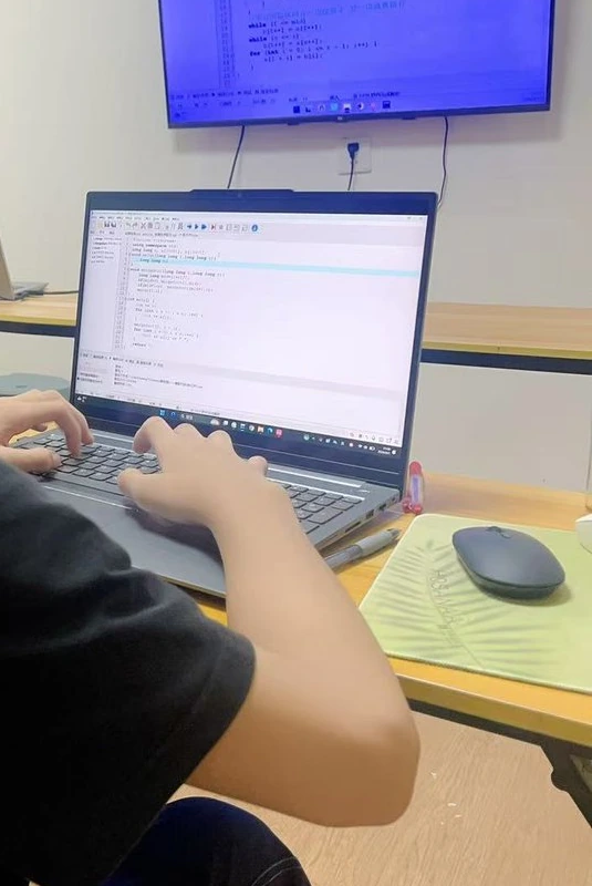 学生用双手输入代码，笔记本与前方屏幕展示编程练习
